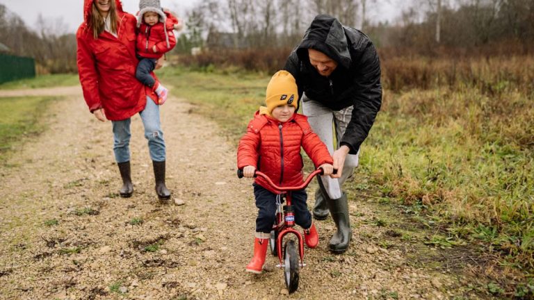 Happy family walking outdoors in fall, teaching child to ride bike.